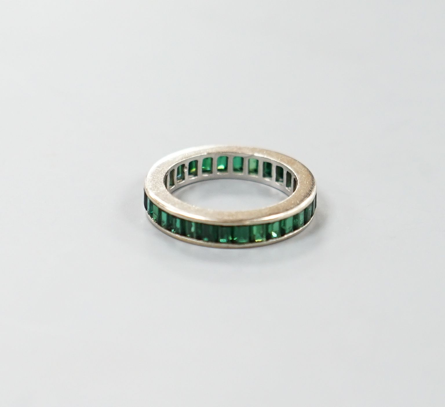 A white metal and green garnet? set full eternity ring, size L, gross weight 3.3 grams.